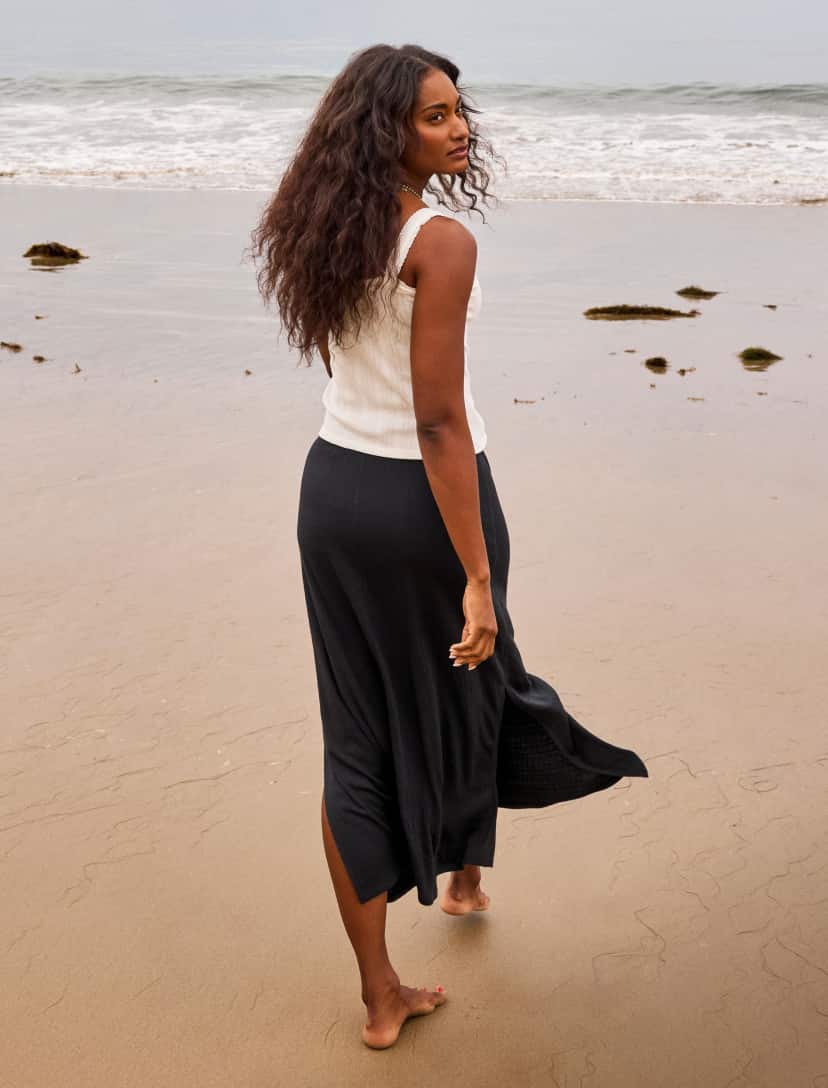 Image of woman on the beach wearing white tank and black skirt.