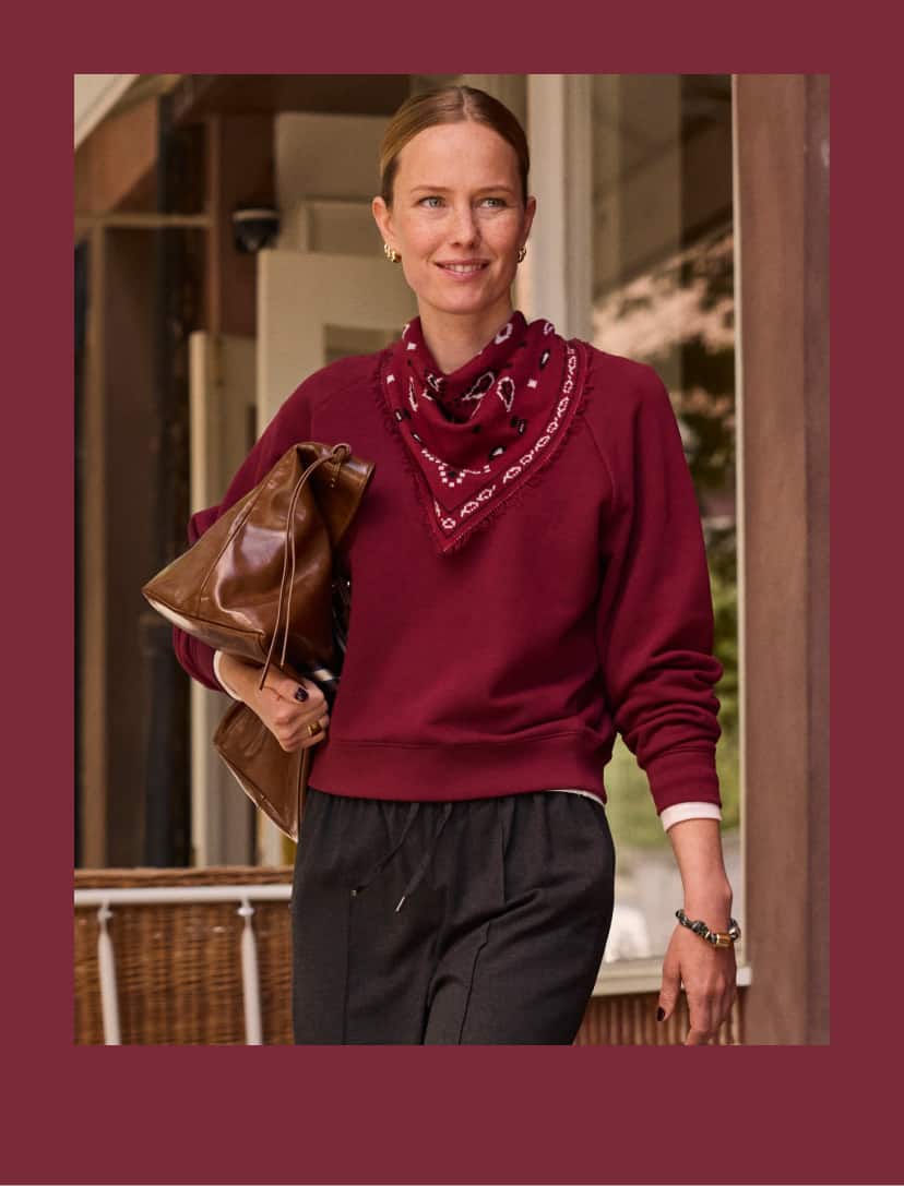 Woman wearing a maroon pullover sweatshirt with a maroon bandana scarf and black pull on pants. 