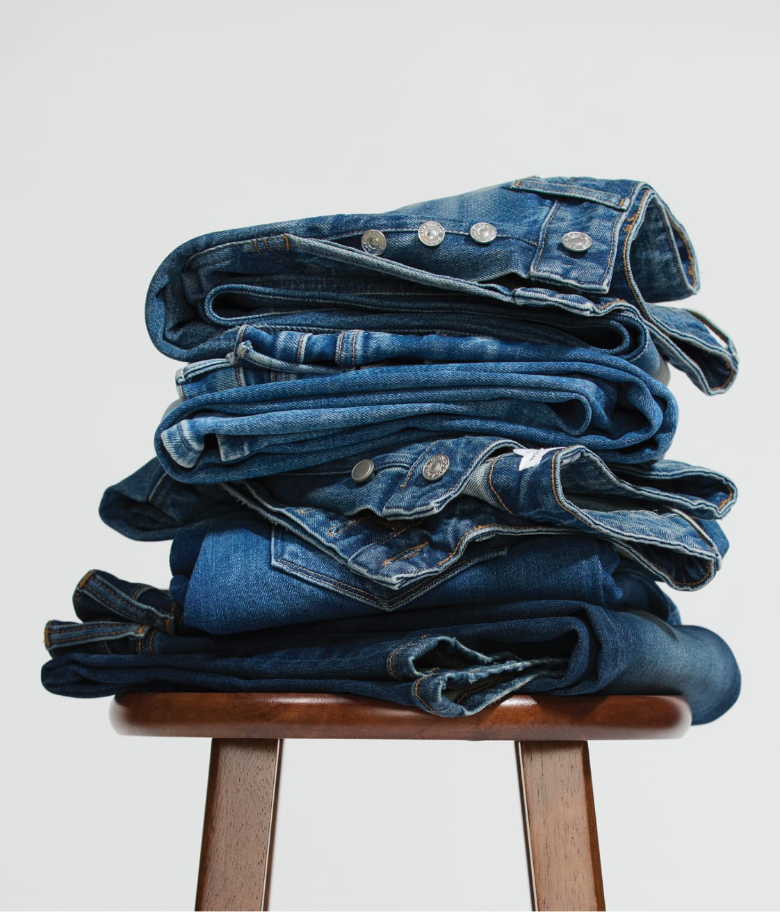 Image of a stack of folded denim on a wooden stool. 