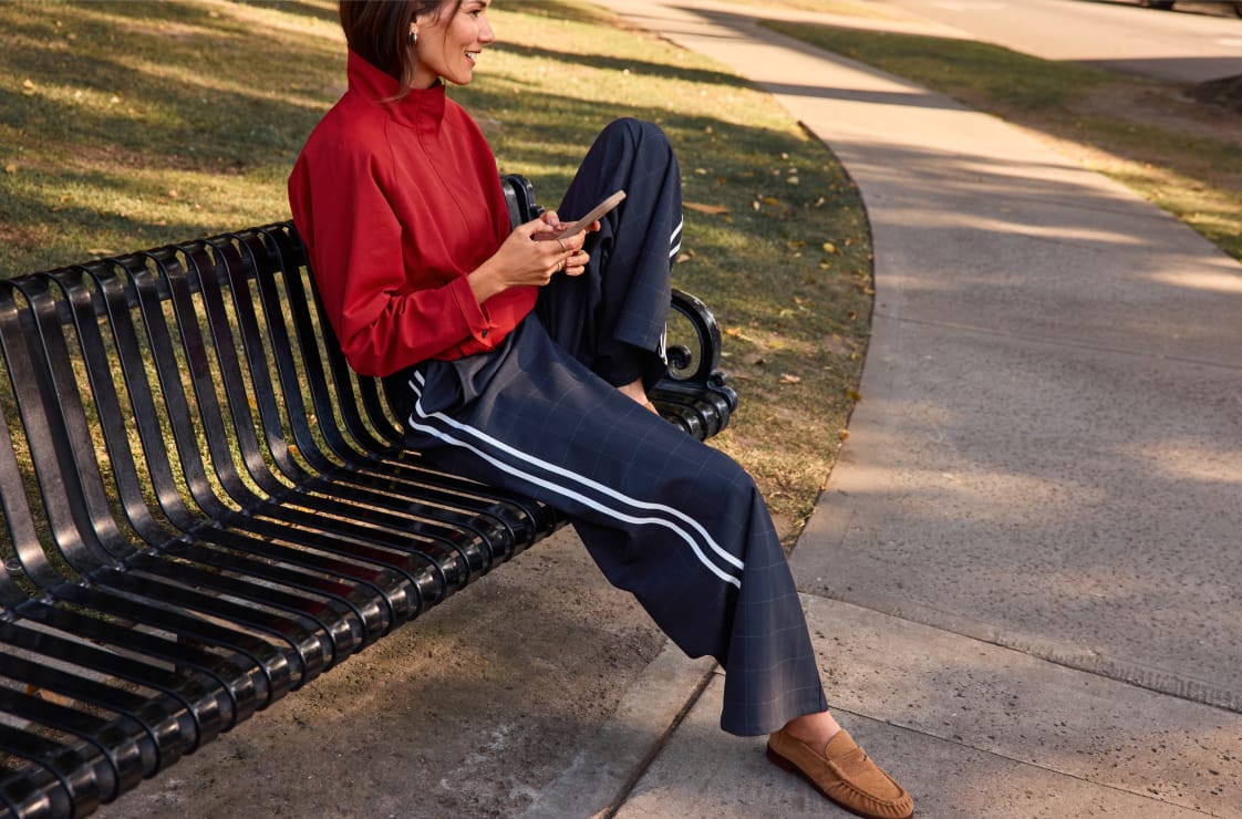 Woman wearing navy windowpane track pants with a red bomber jacket and suede loafers. 