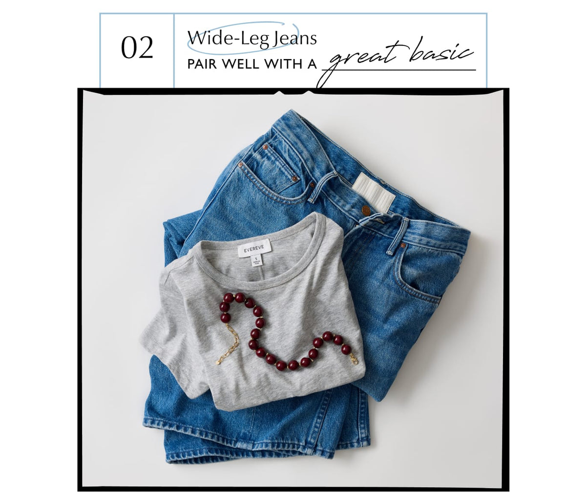 Folded pair of wide leg jeans with a grey tee and beaded necklace.
